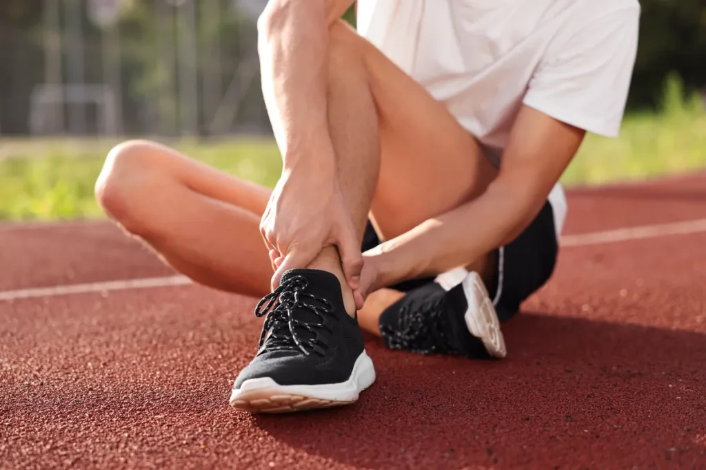 Runner sitting on a track holding an injured ankle